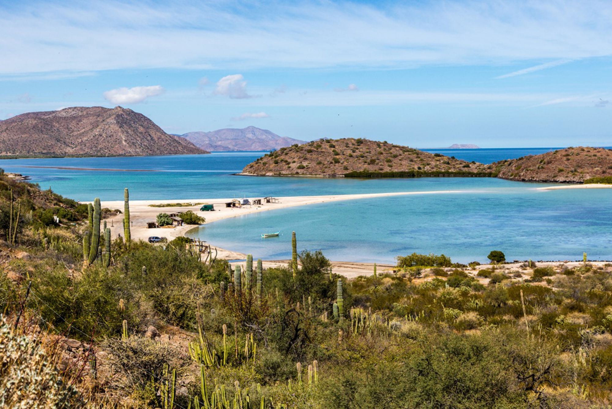 Uitzicht op een turquoise baai met zandstrand, cactussen en heuvels aan de kust van Mexico.