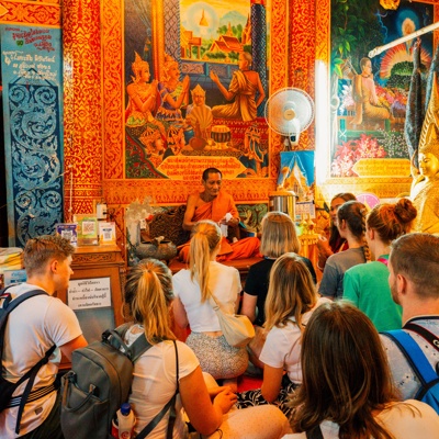Jonge reizigers luisteren naar een boeddhistische monnik in een kleurrijke tempel tijdens een 22-35ers reis Thailand.