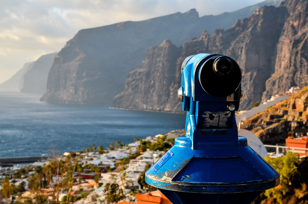 Uitzichtpunt met verrekijker bij de kliffen van Tenerife, met de oceaan en kustdorp op de achtergrond.