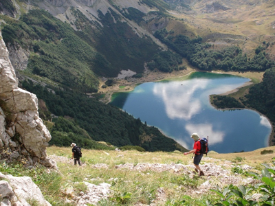 Wandelaars dalen af naar een bergmeer in Bosnië & Herzegovina tijdens de 10-daagse wandelvakantie route.