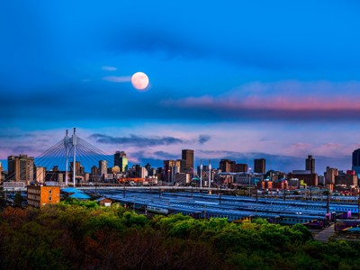 Skyline van Johannesburg bij schemering met brug, treinsporen en volle maan.