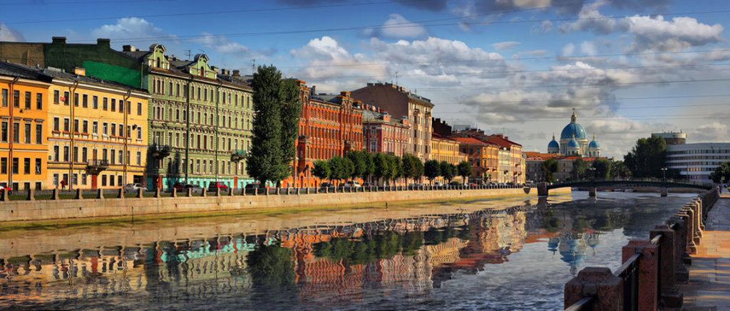 Kleurrijke gevels langs een kanaal in Sint-Petersburg, met op de achtergrond de blauwe koepels van de Drievuldigheidskathedraal.