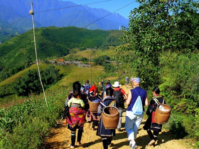 Wandelaars en locals met rieten manden op een bergpad langs rijstterrassen in Noord-Vietnam.