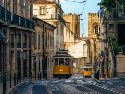 Gele tram in een smalle straat in Lissabon, Portugal, met historische gebouwen op de achtergrond.