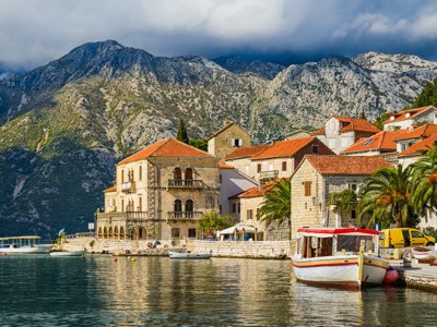 Kustdorp in de Baai van Kotor, Montenegro, met stenen huizen en boten voor een bergachtig decor.