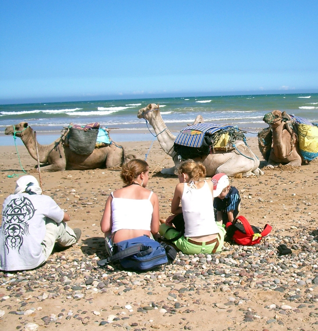 Gezin op het strand in Marokko met kamelen op de achtergrond.