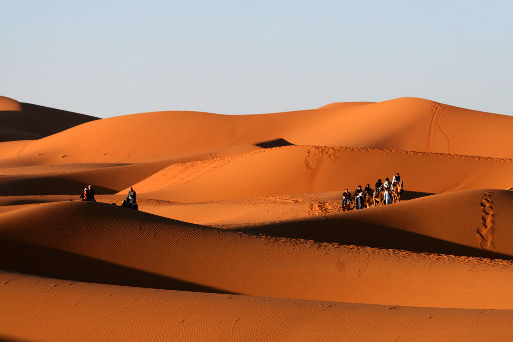 Karavaan met kamelen en reizigers in de Sahara bij Merzouga, Marokko, tussen hoge zandduinen.