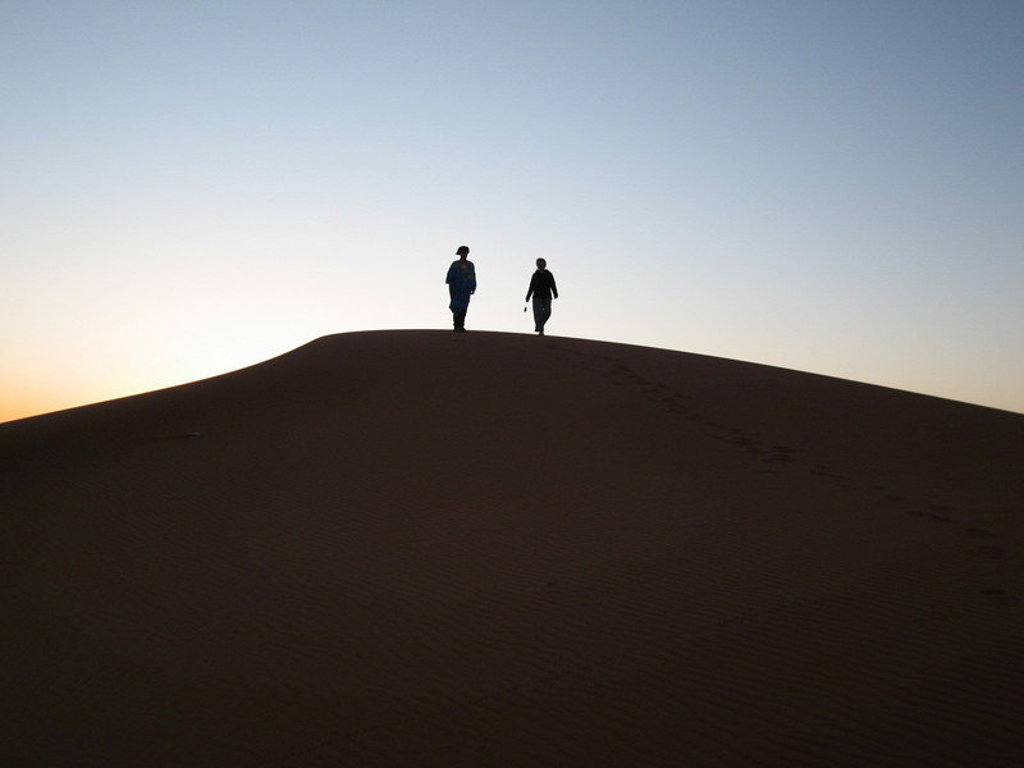 Twee reizigers lopen over een zandduin bij zonsondergang tijdens de groepsrondreis Marokko Chill & Adventure.