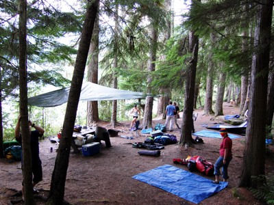 Kampeerplek in het bos langs de Route Canada, met reizigers die tenten en zeilen opzetten.