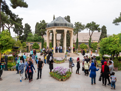 Drukke tuin bij de Hafez-tombe in Shiraz, Iran, met achthoekig paviljoen en bloemenperken.
