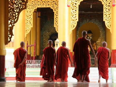 Monniken in rode gewaden lopen door een tempel met gouden zuilen in Myanmar tijdens de 25-daagse route Birma.