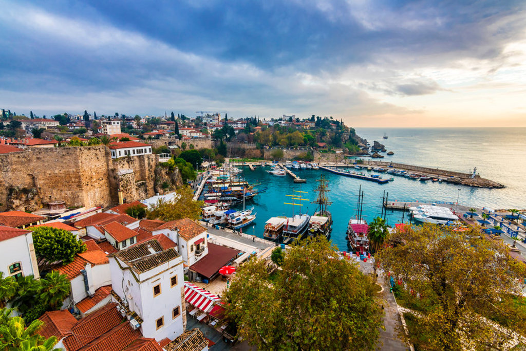 Uitzicht op de haven van Antalya met jachten, oude stadsmuren en de Middellandse Zee bij zonsondergang.