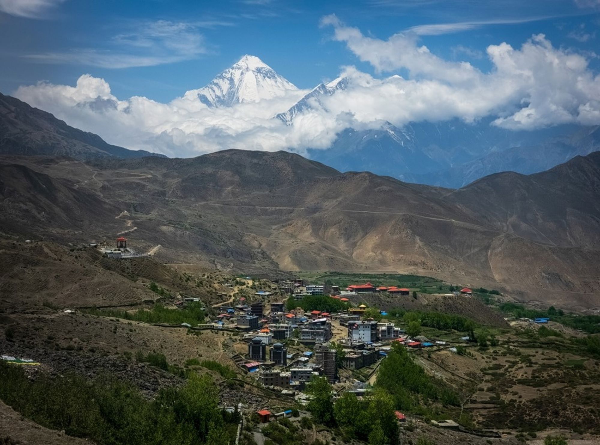 Dorp in de Himalaya in Nepal met besneeuwde bergtoppen en wolken op de achtergrond.