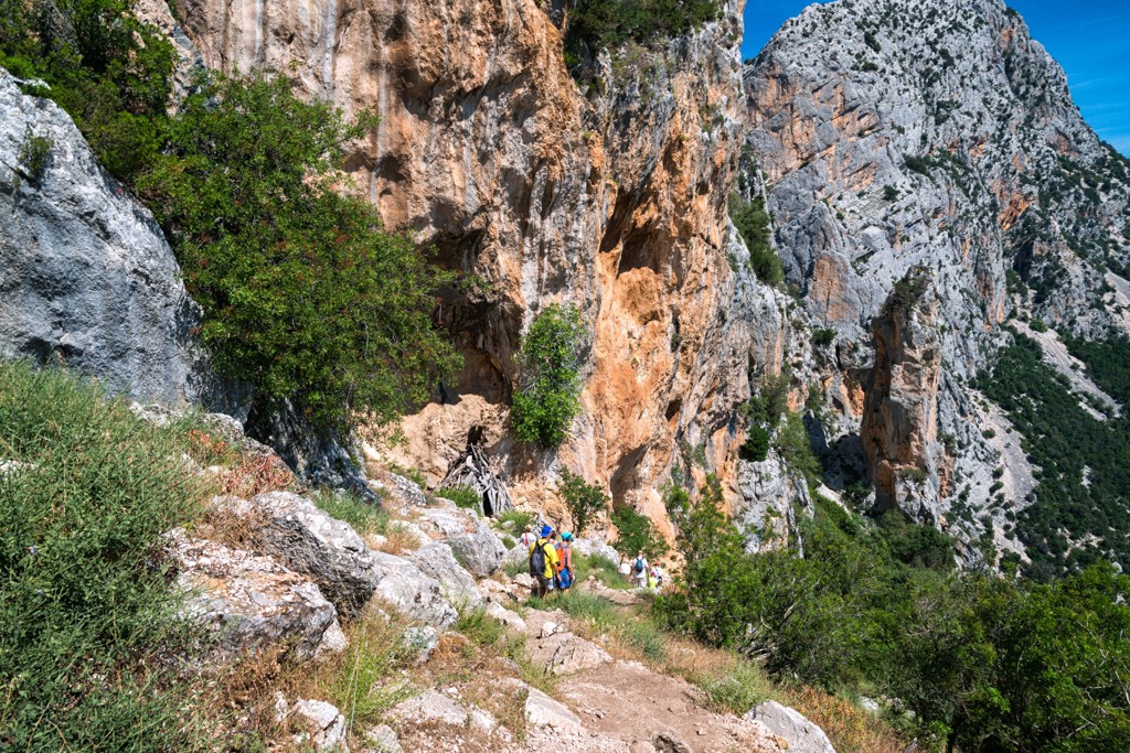 Wandelaars op een bergpad langs steile rotswanden tijdens een wandelvakantie op Sardinië, Italië.