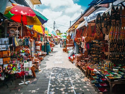 Souvenirmarkt op Bali met kleurrijke parasols en kraampjes vol houtsnijwerk, textiel en peddels.