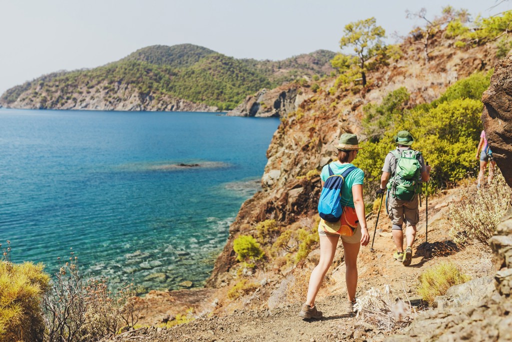 Wandelaars op een kustpad langs de Turquoise Kust in Turkije, met uitzicht op helderblauw zeewater.
