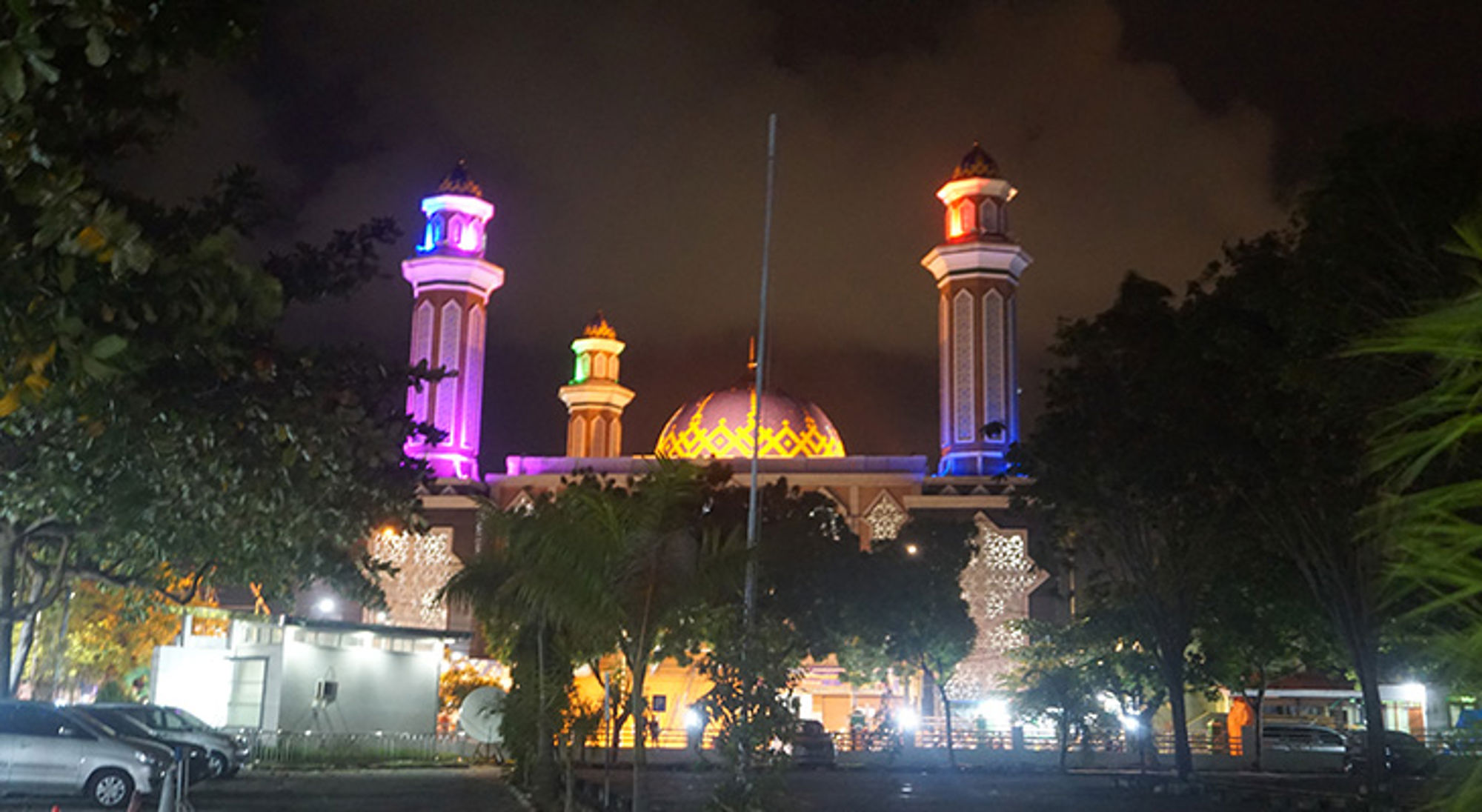 Verlichte moskee met gouden koepel en minaretten in kleurrijke verlichting bij nacht.
