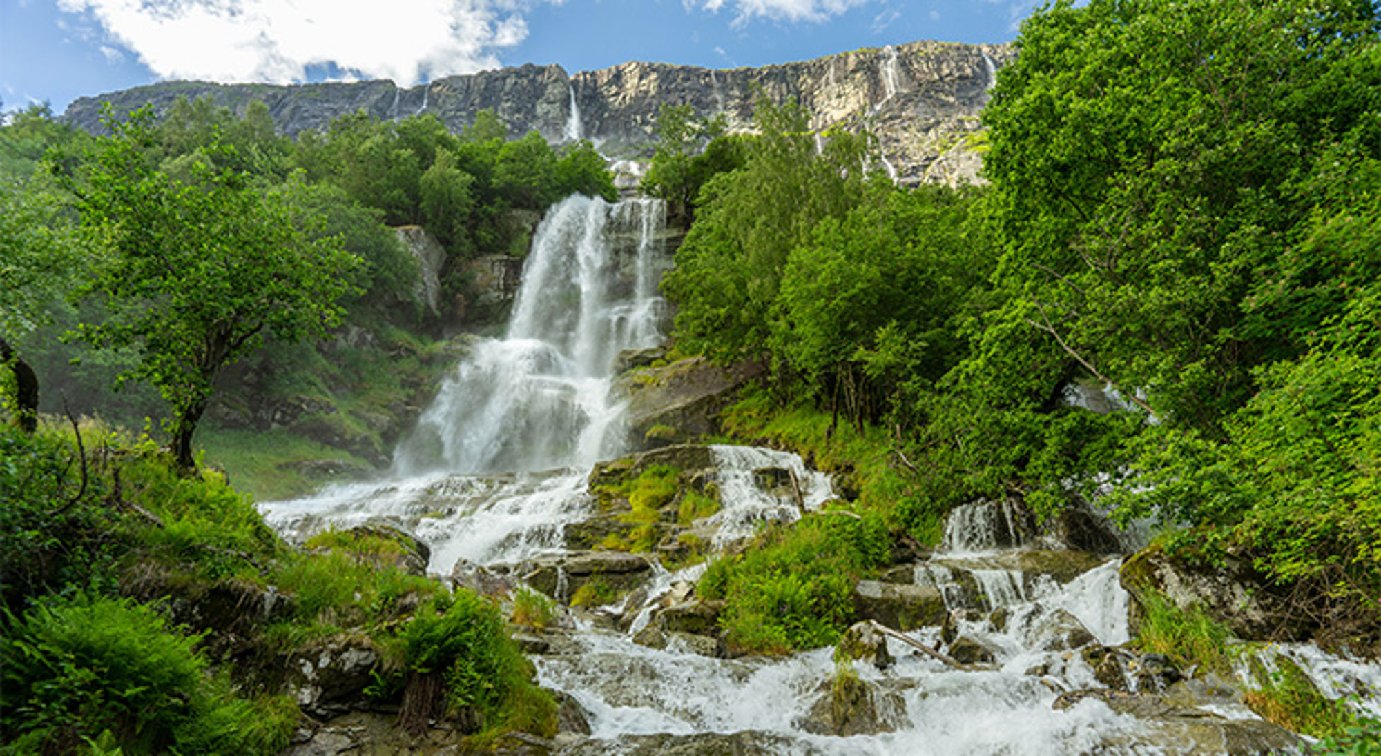 Vinnufossen waterval in Noorwegen Waterval die in meerdere treden door een groen berglandschap stroomt, met rotswand op de achtergrond.