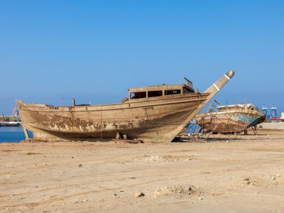 Traditionele houten dhow op het droge bij de kust van Saoedi-Arabië, met havenkranen op de achtergrond.