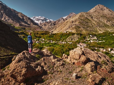 Wandelaar kijkt uit over een Berberdorp in de Atlas met besneeuwde toppen bij de beklimming van Mt. Toubkal.