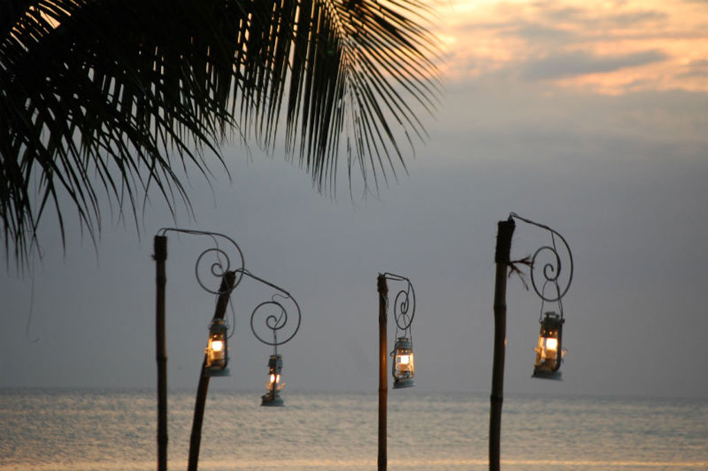 Lantaarns aan palen bij zee tijdens zonsondergang, met palmtak in beeld op Zanzibar.