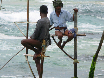 Steltvissers op houten palen in de branding aan de kust van Sri Lanka.
