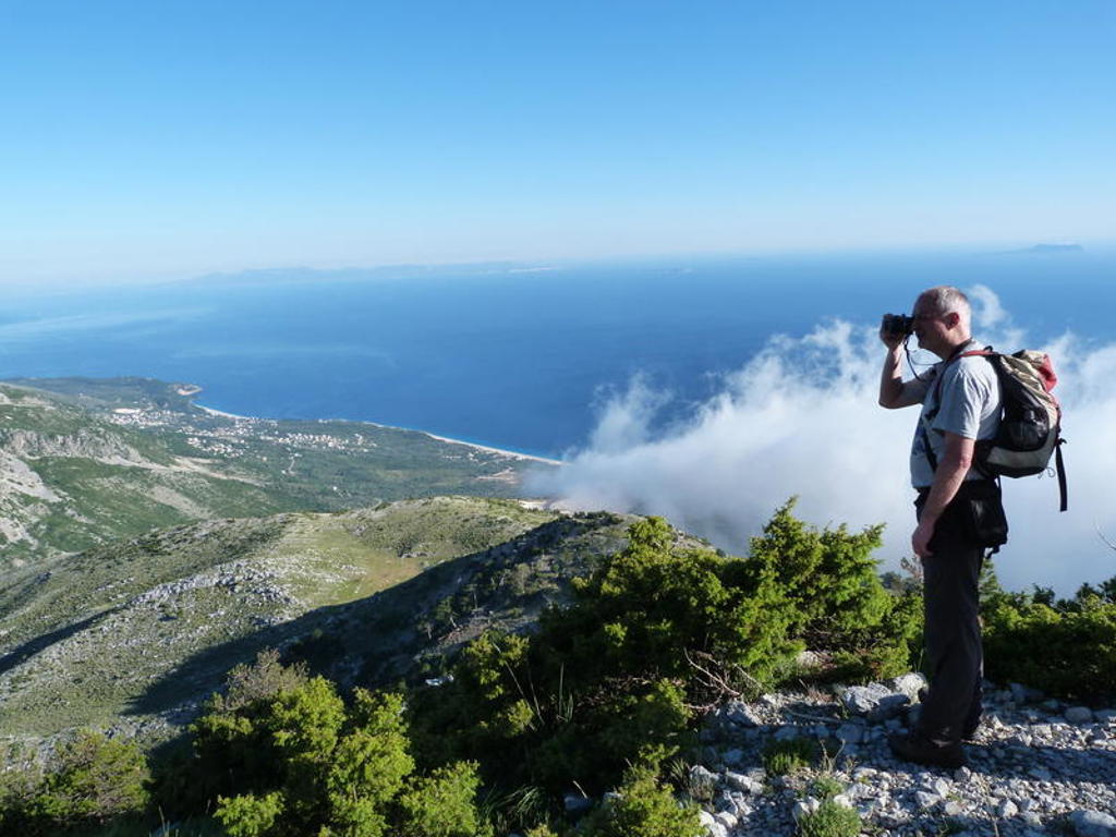 Wandelaar met verrekijker op bergtop met uitzicht op de Albanese kust en de Ionische Zee.