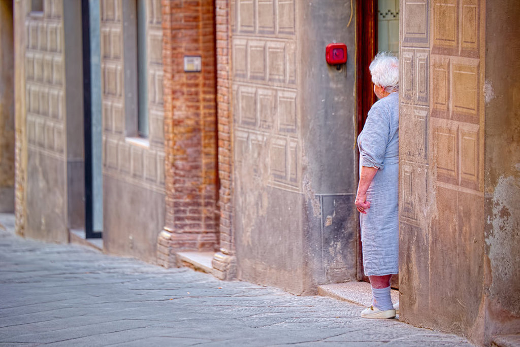 Oudere vrouw staat in een deuropening in een smalle straat in Toscane, Italië.