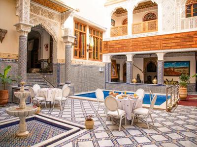 Binnenplaats van een riad in Marokko met mozaïektegels, fontein, zwembad en ontbijttafel.