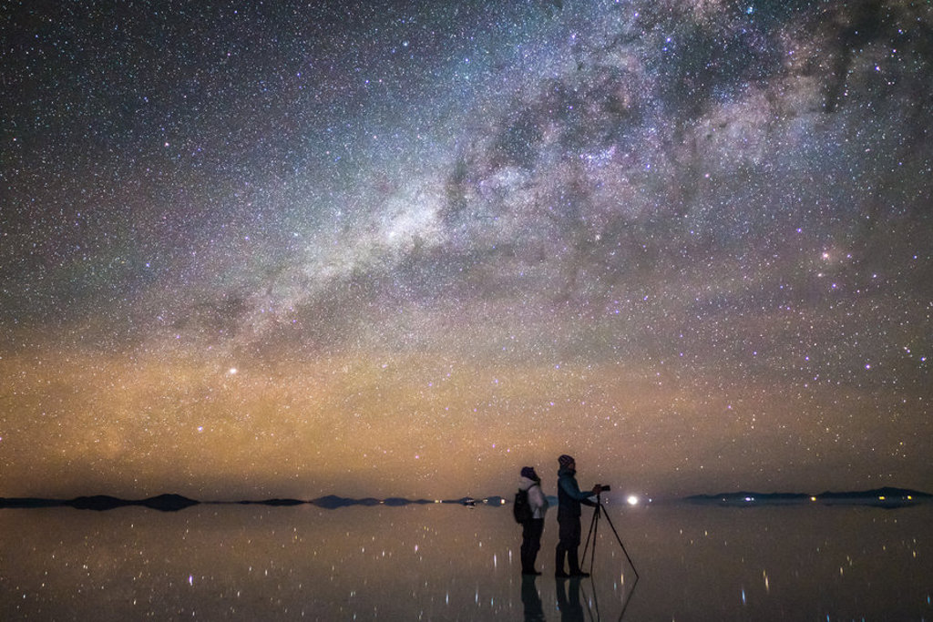 Sterrenhemel en Melkweg boven de Salar de Uyuni in Bolivia, met twee reizigers op de zoutvlakte.