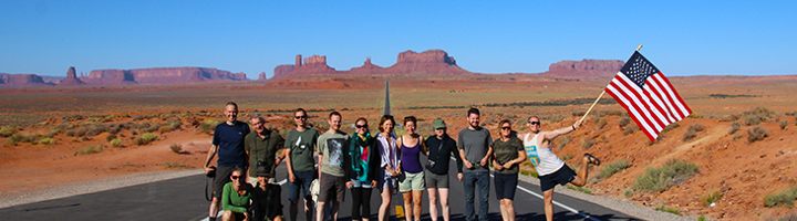 Groepsreis door Noord-Amerika: reizigers poseren op een weg in Monument Valley met Amerikaanse vlag.
