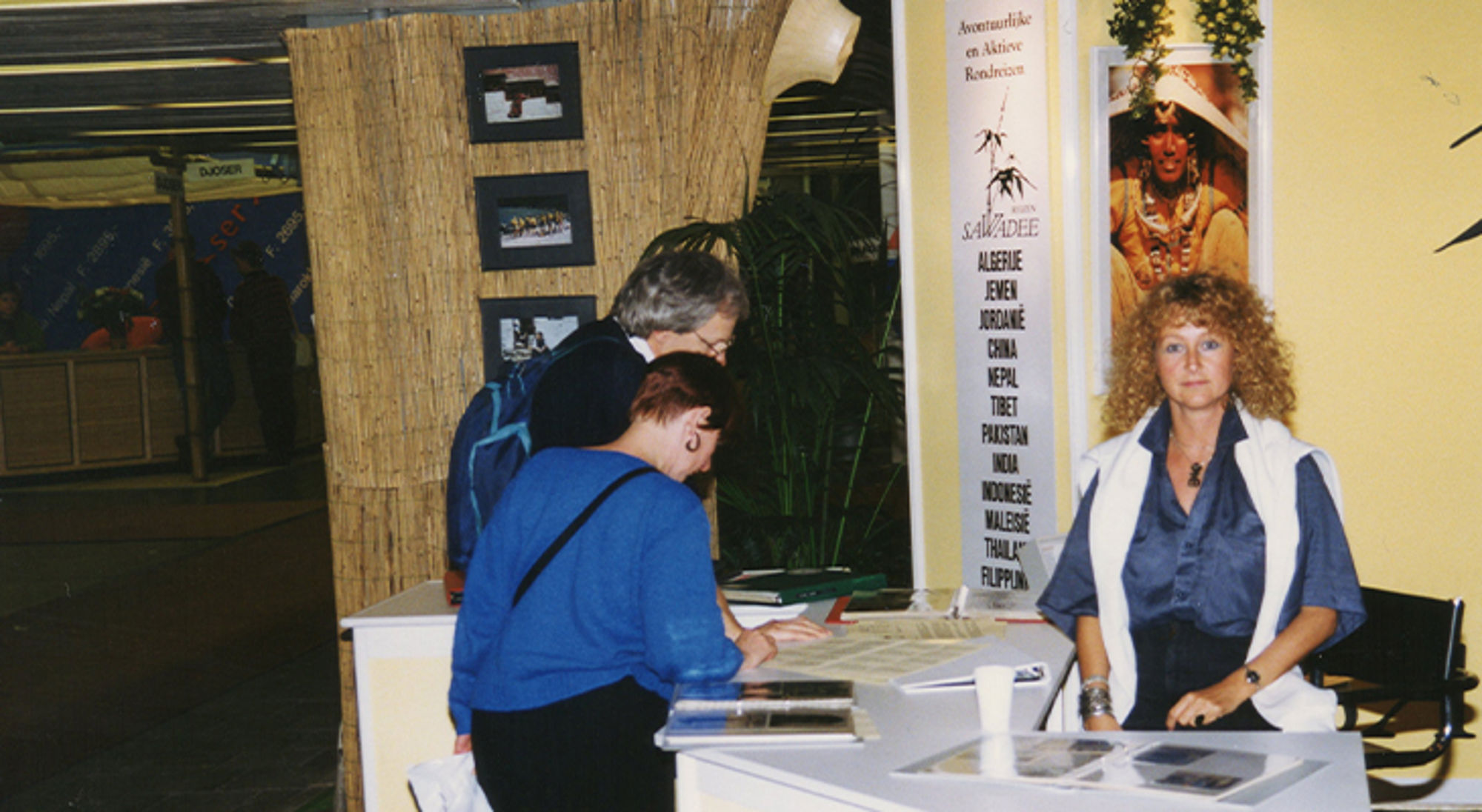 Mieke op de Vakantiebeurs Reisbeursstand met bezoekers bij een informatiestand en medewerkster achter de balie.
