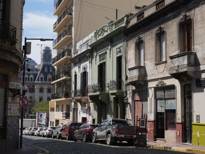 Straat in Buenos Aires met kleurrijke historische gevels en geparkeerde auto’s langs de stoep.
