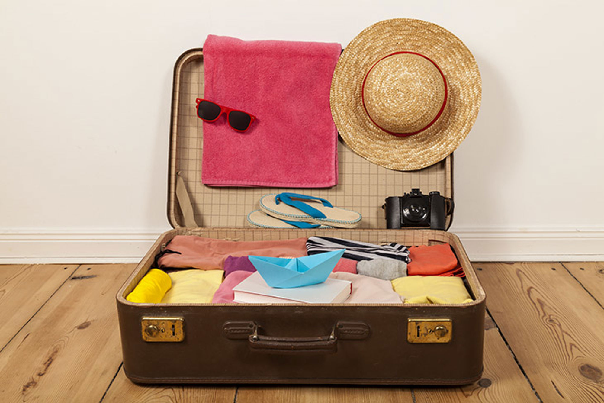 Open koffer met vakantiespullen zoals kleding, zonnebril, strohoed, slippers en camera.
