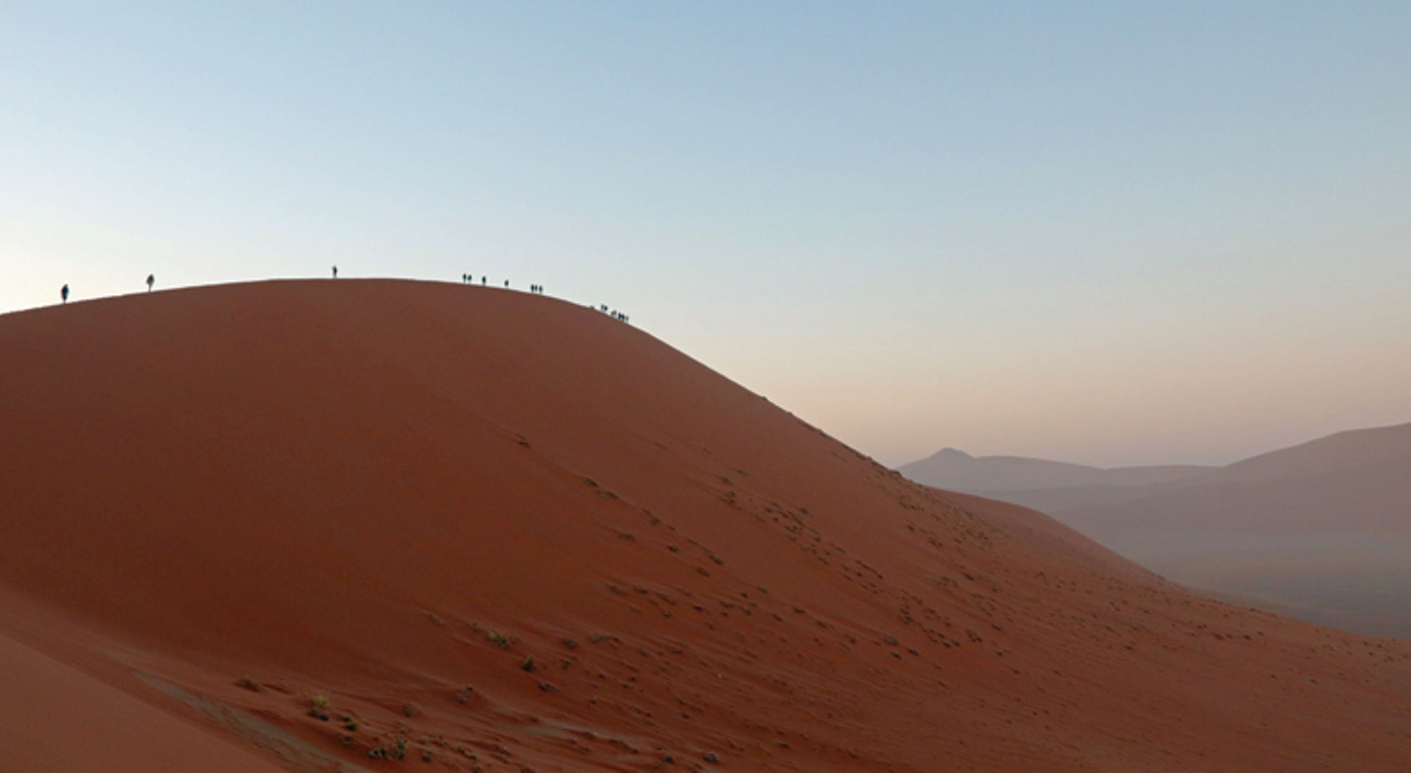 woestijn zand heuvel in namibie Wandelaars op de kam van een hoge rode zandduin bij zonsopkomst.