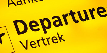 Gele luchthavenbord met “Departures” en “Vertrek” als verwijzing naar wachttijden op Schiphol.