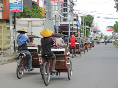Becaks (fietstaxi’s) rijden door een drukke straat in Indonesië tijdens de route Bali & Sulawesi.