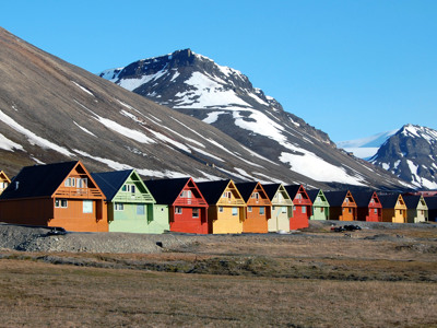Gekleurde houten huizen in Longyearbyen op Spitsbergen, met besneeuwde bergen op de achtergrond.