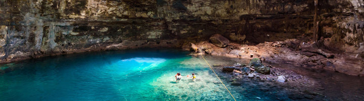 Cenote met helderblauw water in een grot, waar bezoekers zwemmen.