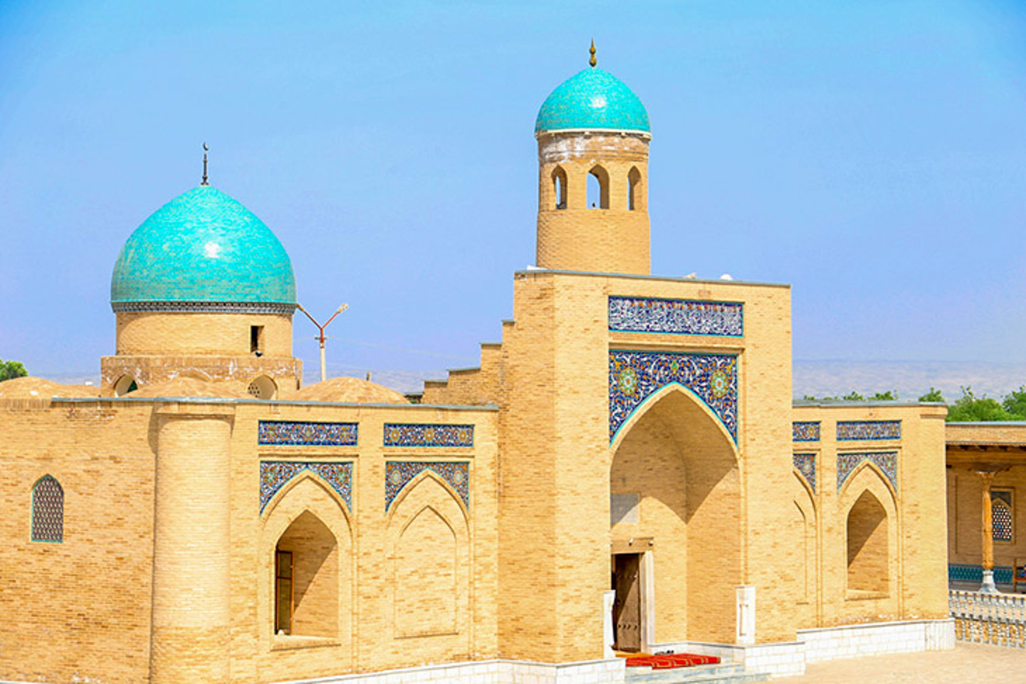 Paleis in Oezbekistan Moskee met turquoise koepels en minaret, met kleurrijke tegelmozaïeken rond de entree.