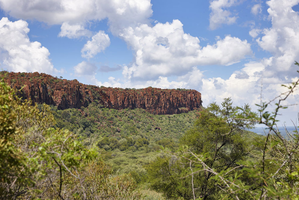 Rotsplateau boven groen savannelandschap in Namibië, met wolkenlucht.