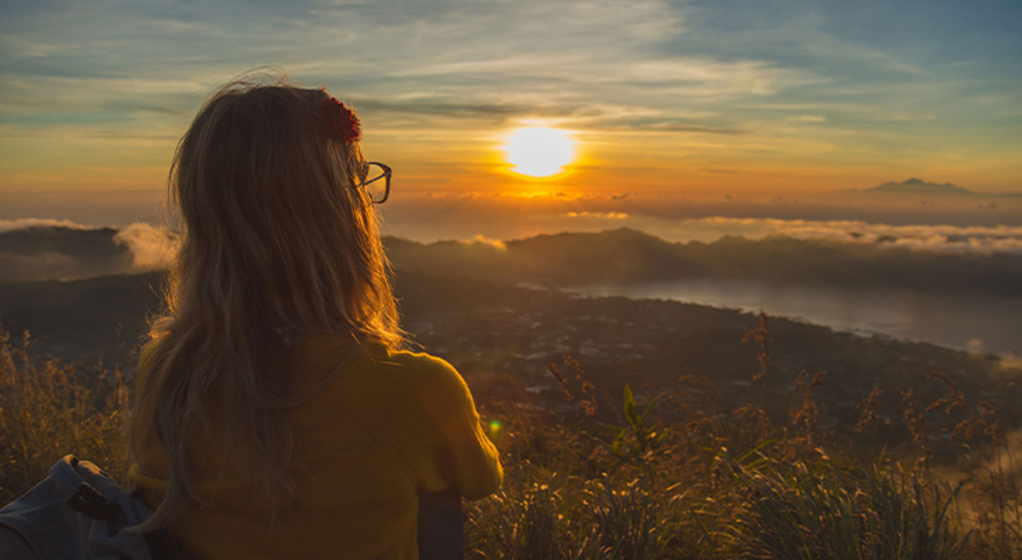 Mount Batur Bali Vrouw kijkt bij zonsopkomst uit over bergen en mistige vallei vanaf een uitkijkpunt.