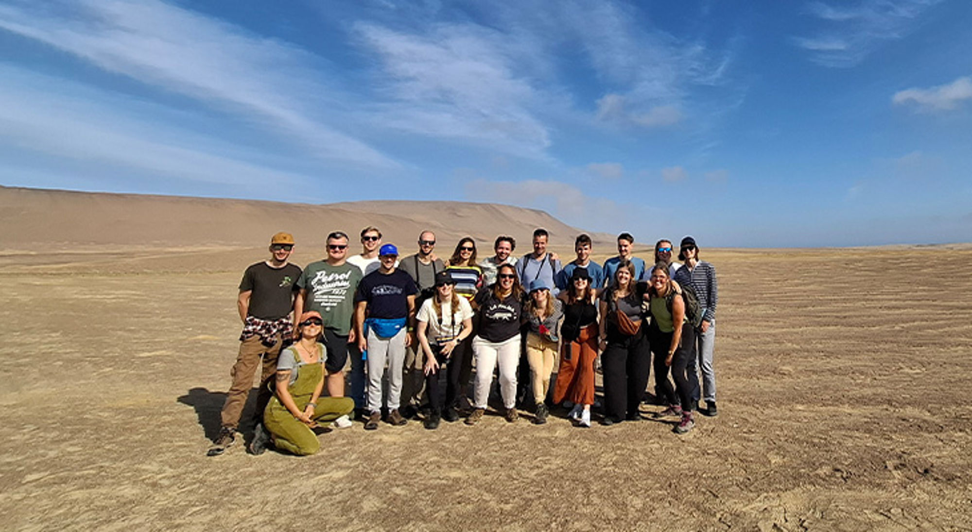 Jongerenreis Peru Groepsfoto van reizigers in een uitgestrekt woestijnlandschap met duinen op de achtergrond.