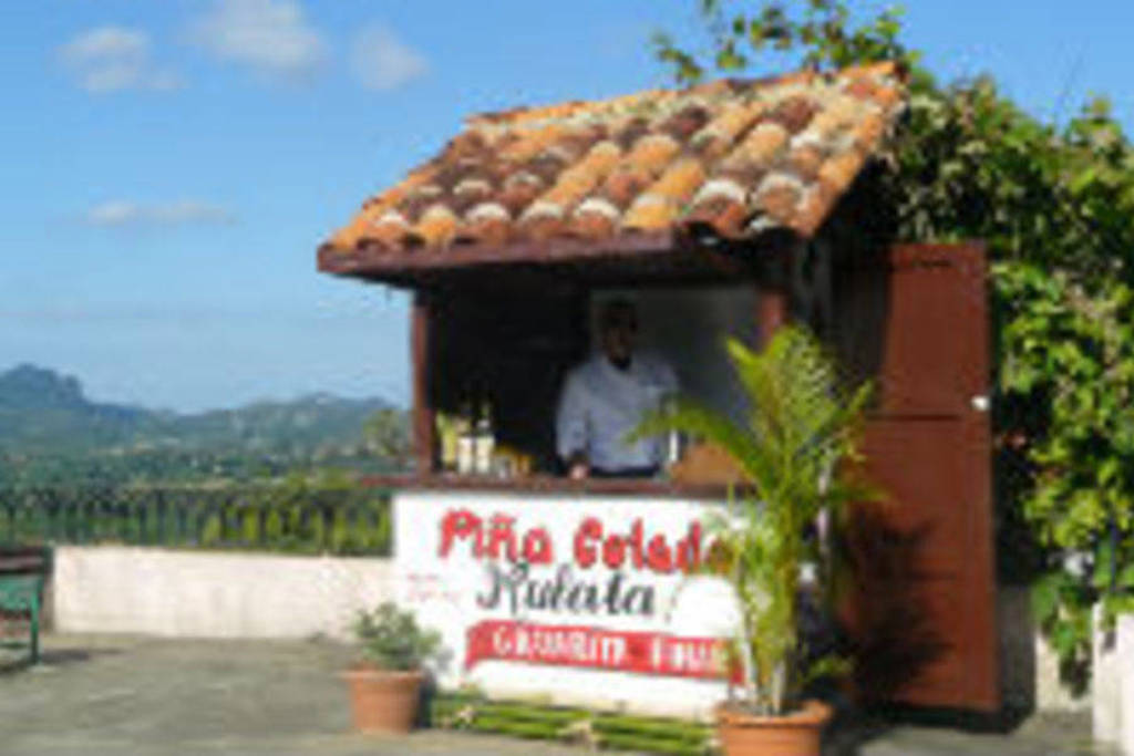 Kleine bar met bord “Pina Colada Natural” op een terras met uitzicht op het groene berglandschap van Cuba.