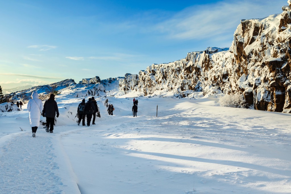 Groepsrondreis IJsland winter: wandelaars in besneeuwd lavalandschap met rotswanden onder blauwe lucht.
