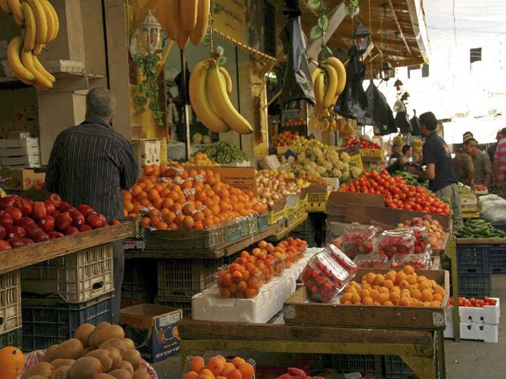 Fruit- en groentemarkt in Jordanië met bananen, sinaasappels en tomaten bij kraampjes.