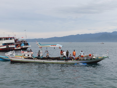 Houten vissersboot met bemanning op zee bij Sulawesi, met bergen op de achtergrond.
