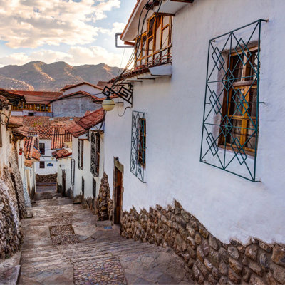 Straatje met witte huizen en rode daken in Cusco, Peru, met bergen op de achtergrond.