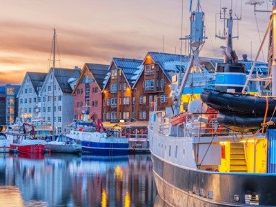 Haven van Tromsø met aangemeerde boten en kleurrijke houten huizen bij zonsondergang, Noorwegen.