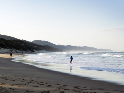 Rustig strand aan de Wild Coast in Zuid-Afrika met golven, duinen en wandelaars langs de waterlijn.